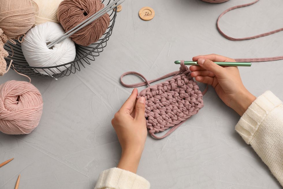 how to fasten off in crochet, woman crocheting with threads at gray table