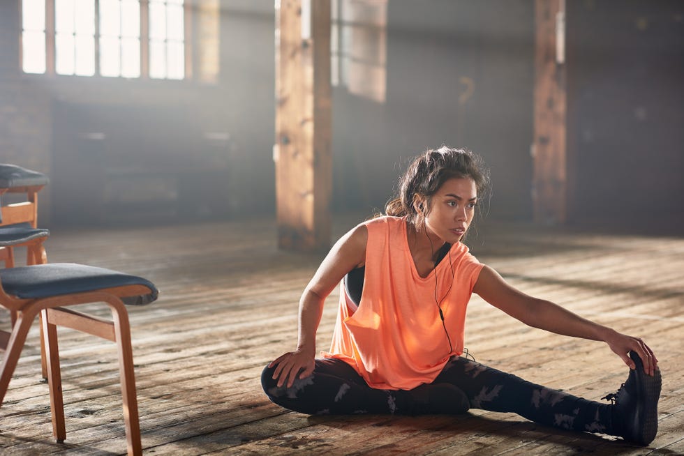 young woman with earbuds stretching on wooden floor in sunny gym