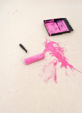 paint roller and tray with pink paint spilled on a cream rug