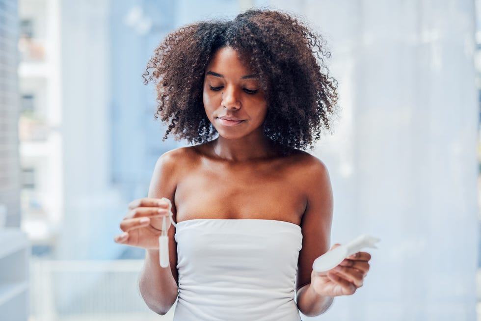 shot of a young woman holding up a tampon and a sanitary pad in the bathroom at home