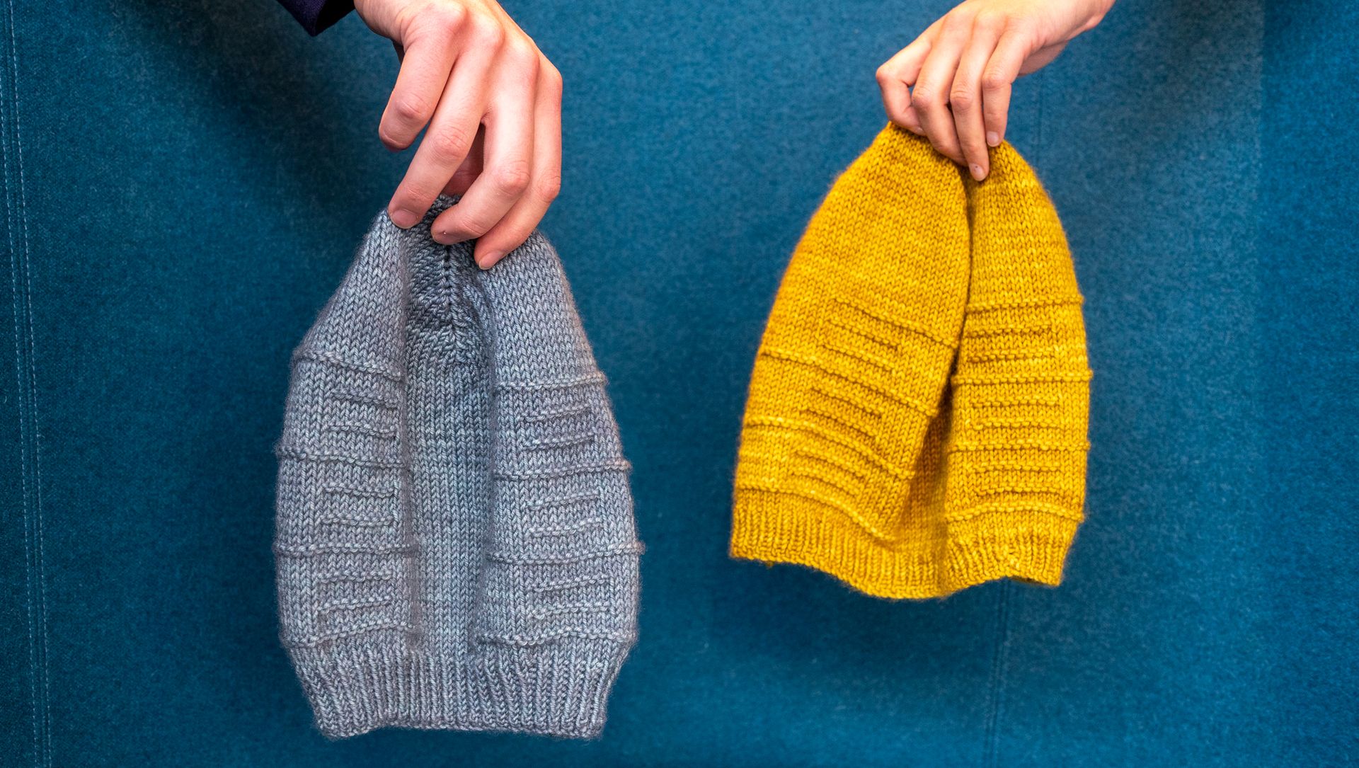 hands holding grey and yellow knit beanies
