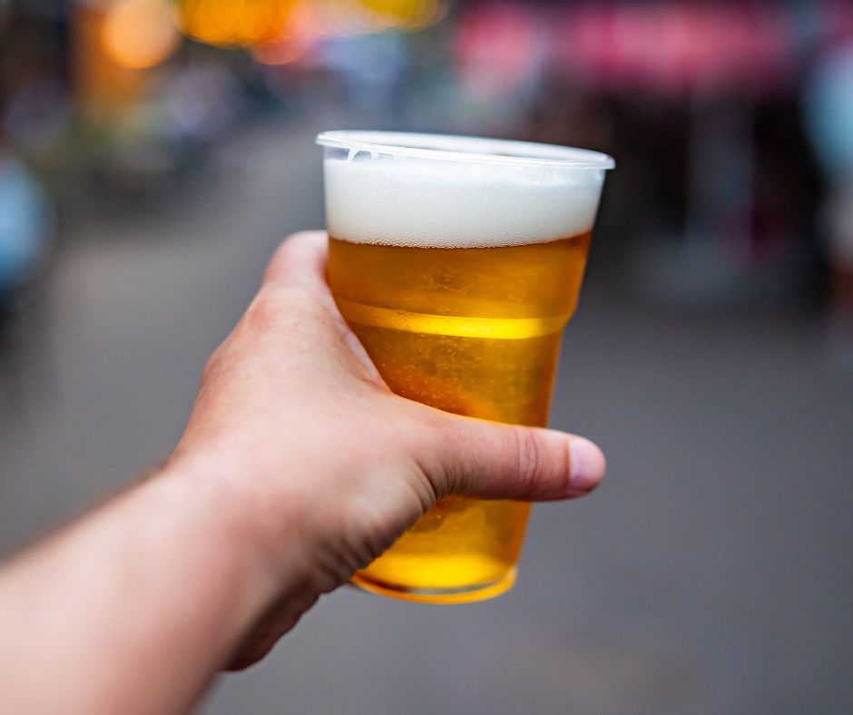a person holding a transparent cup of beer with a foamy top