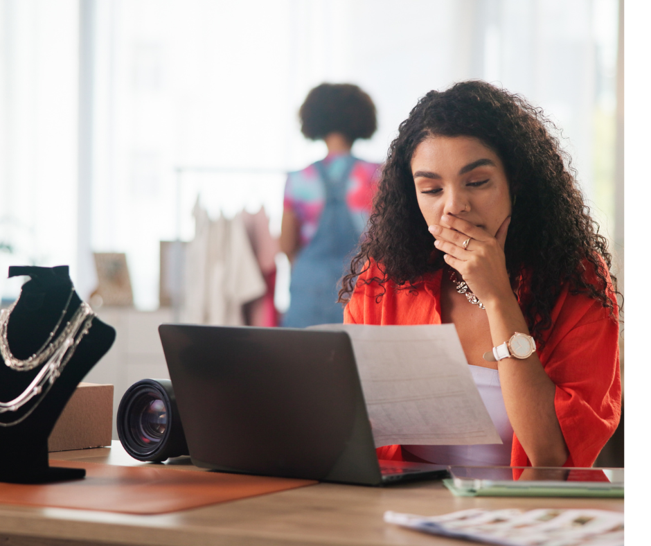 a woman reviewing documents at a desk with jewelry and a camera lens nearby