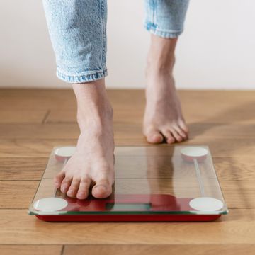 cropped shot of young barefoot woman in casual blue jeans stepping onto floor scales to check her weight