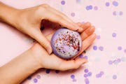 how to make bath bombs, flat lay of a bath bomb in girls hand with festive confetti