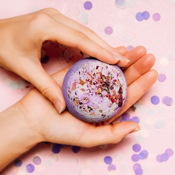 how to make bath bombs, flat lay of a bath bomb in girls hand with festive confetti