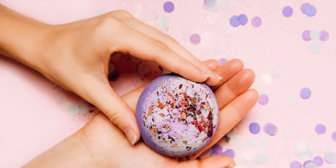 how to make bath bombs, flat lay of a bath bomb in girls hand with festive confetti