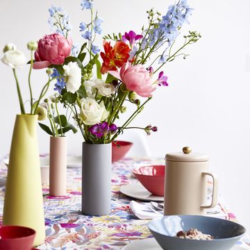 dinning room tabel with a colurful table cloth bowls cups and vases full of flowers on the table