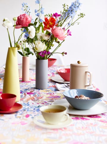 dinning room tabel with a colurful table cloth bowls cups and vases full of flowers on the table