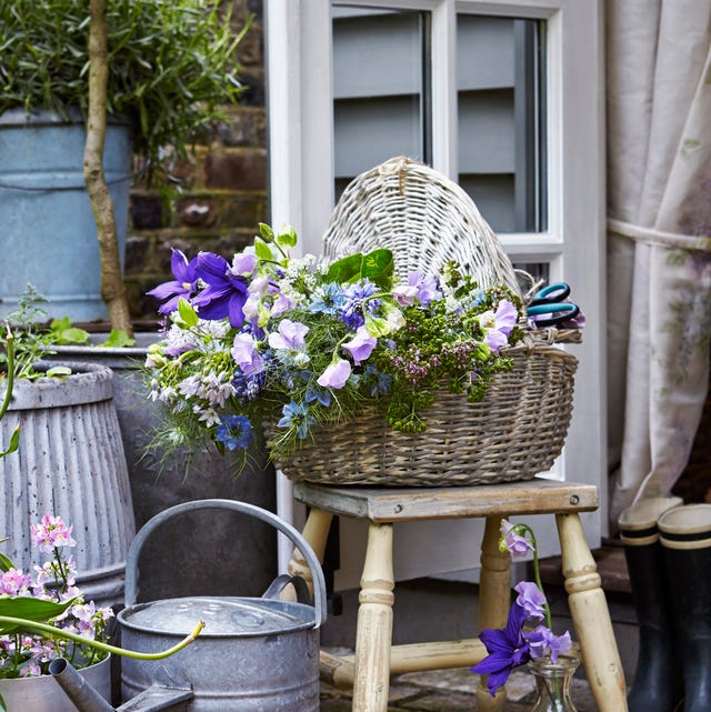cut flowers in wicker basket, nigella, sweetpeas, stool, watering can, glass bottle as vase, paved patio or terrace, watering can, arrangement
