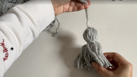how to make a yarn tassel, woman's hand holding a gray tassel