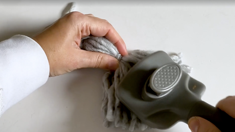 how to make a yarn tassel, woman's hands brushing a gray tassel