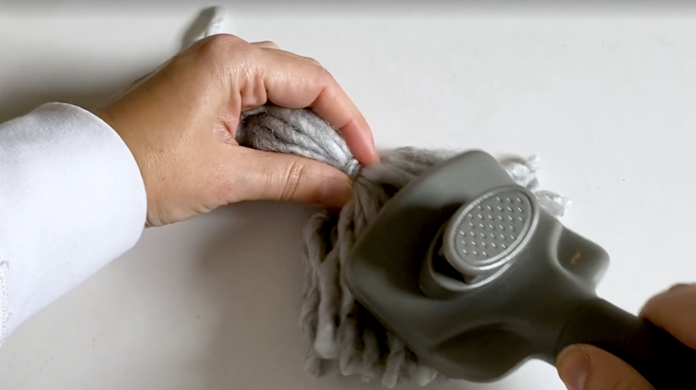 how to make yarn tassel, woman's hands brushing a gray tassel