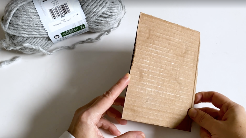 how to make yarn tassel, woman holding a rectangular piece of cardboard