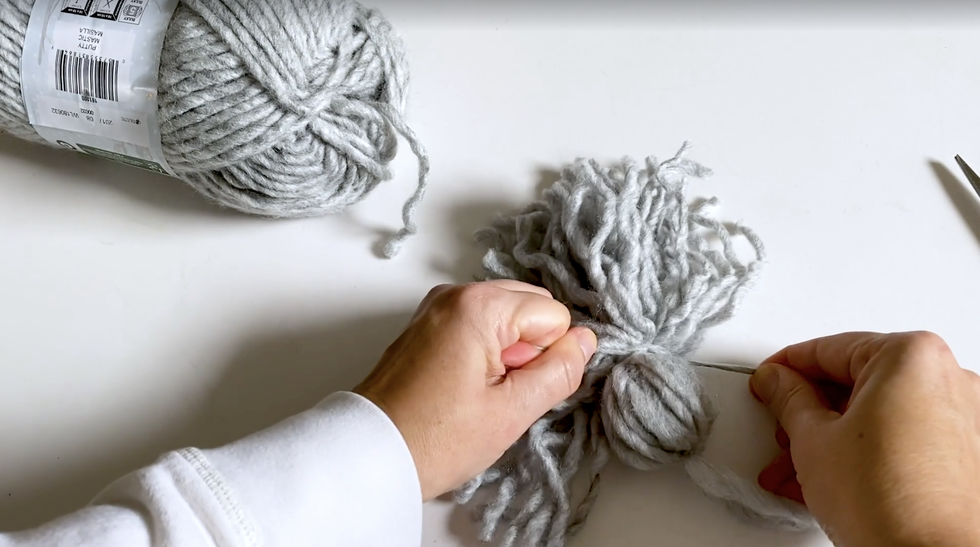 how to make yarn tassel, woman's hands tie a knot on gray tassel