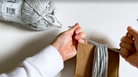 how to make yarn tassel, woman's hands knotting top of gray tassel on cardboard