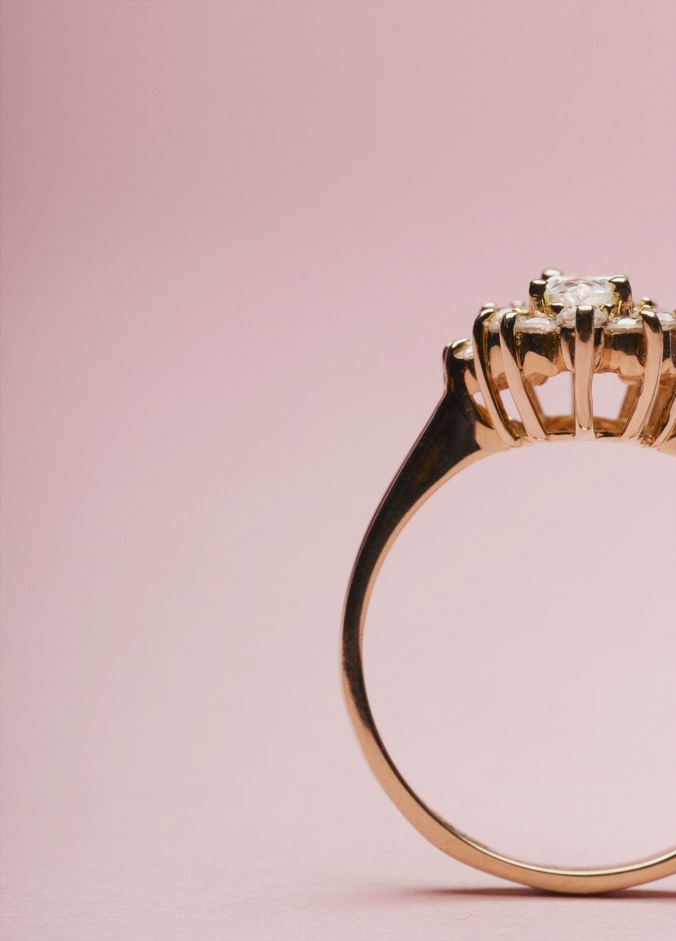a gold diamond engagement ring on a pink background