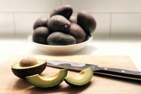 cutting board with avocado, knife, and bowl of avocados