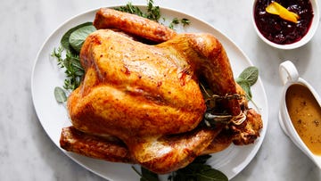 roasted turkey on a platter with fresh herbs, gravy, and cranberry sauce