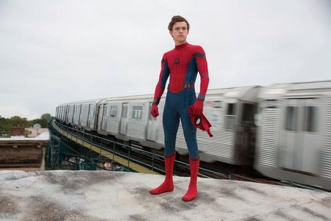 spider man stands before a passing train in a scene from spider man homecoming, the 16th movie if you want to watch all the marvel movies in order