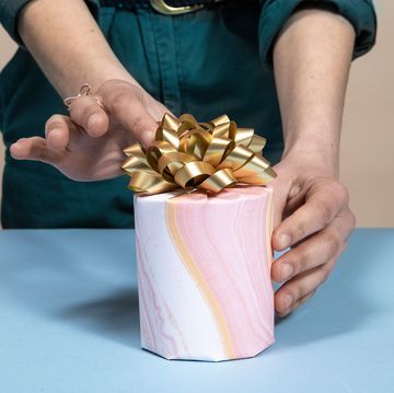 hands adjusting gold bow on gift wrapped candle