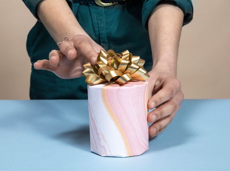 hands adjusting gold bow on gift wrapped candle