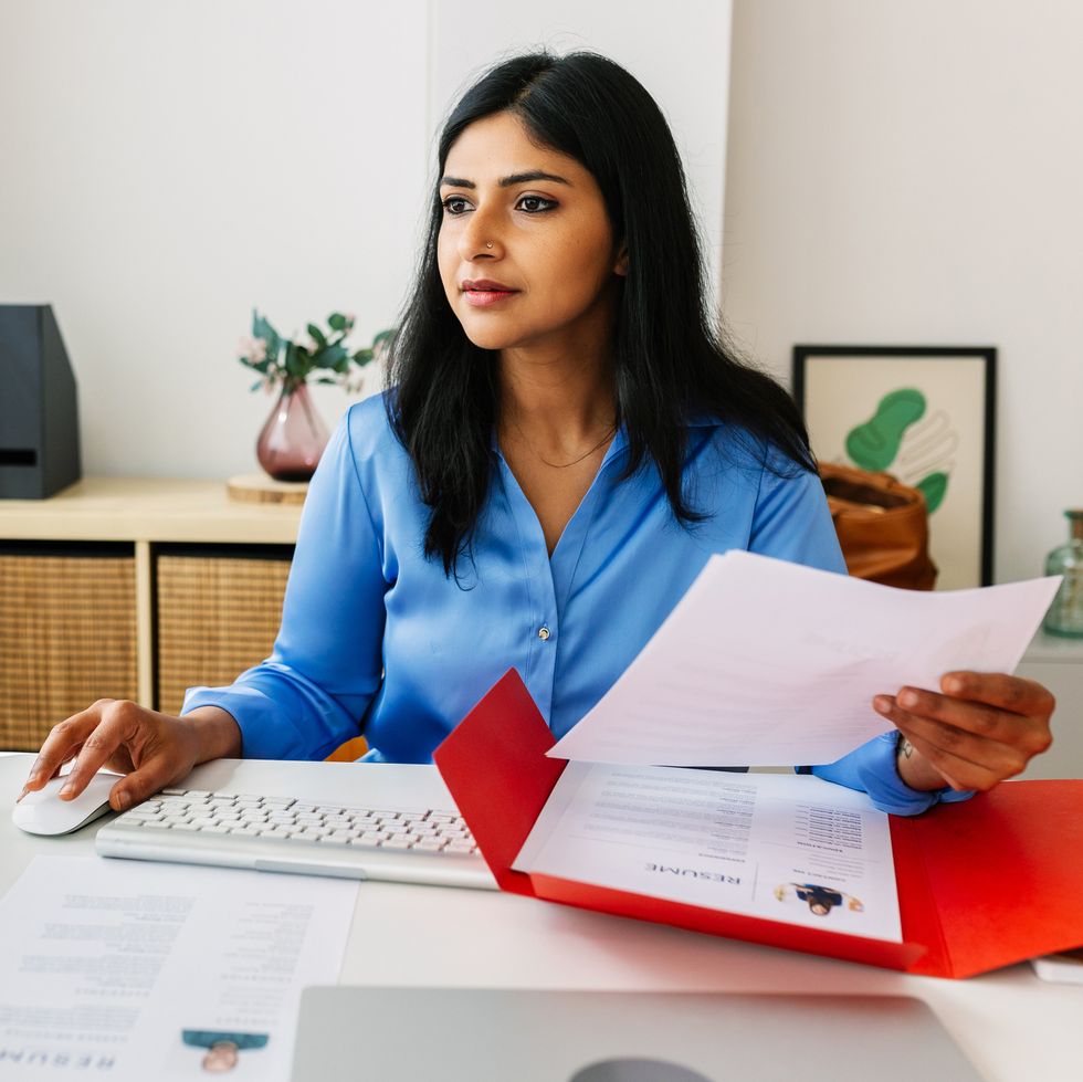 young indian woman holding a cv and looking at a computer screen