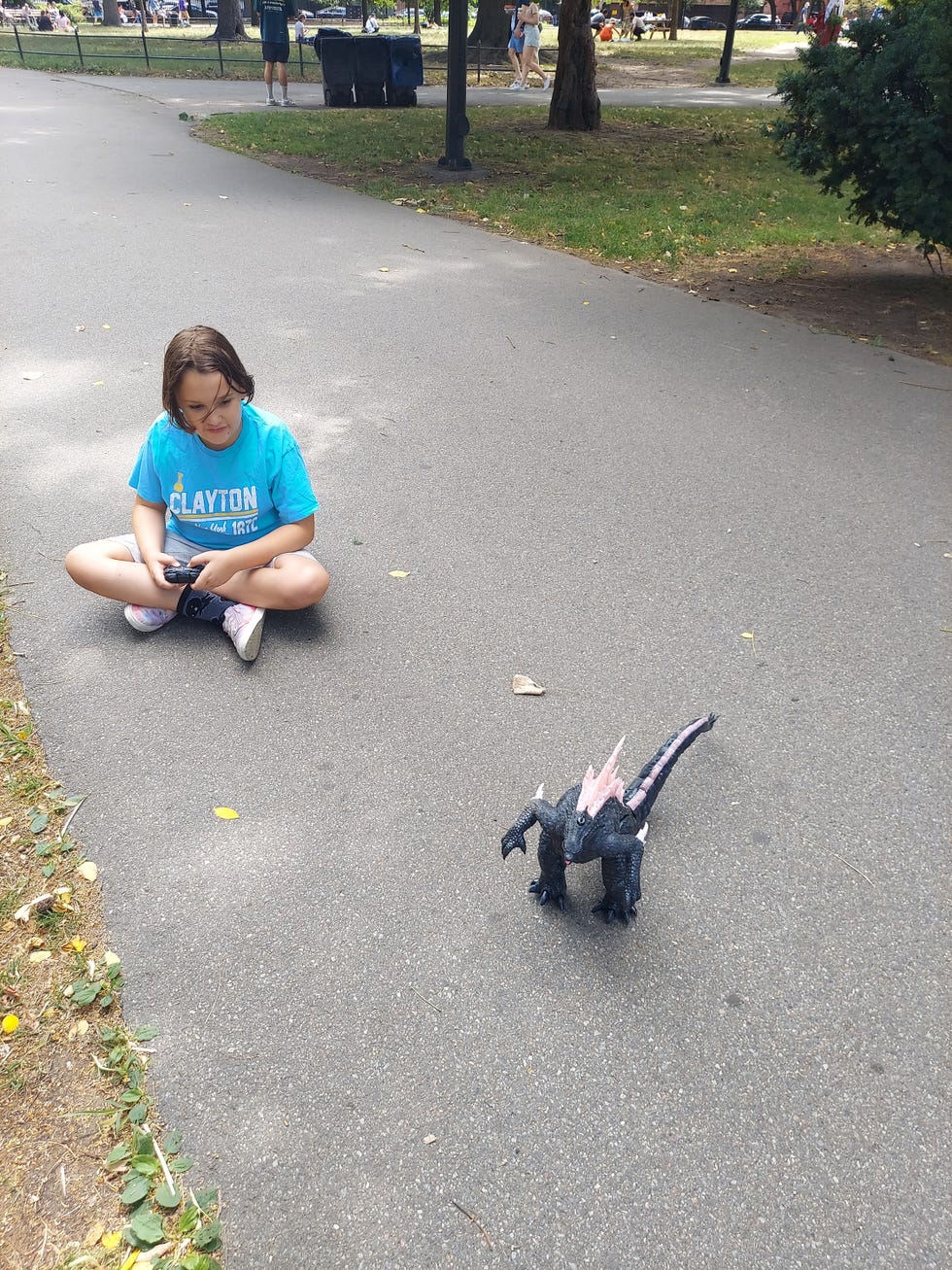 an 8 year old girl tests out a remote controlled godzilla in a city park