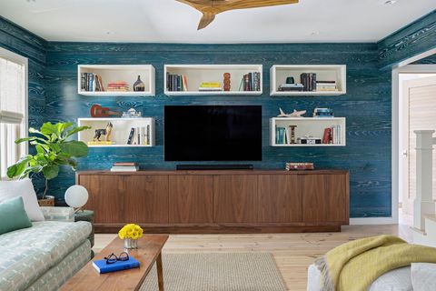 living room, blue wall covering, blue wallpaper, media console with hd tv sitting ontop, wooden ceiling fan, white cubby holes