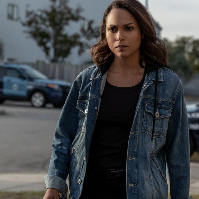 monica raymund stands in front of two police cars wearing a jean jacket
