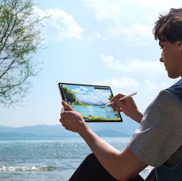 a man sitting down in front of a river drawing using a huawei tablet