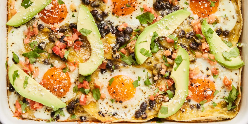 huevos rancheros casserole in a baking dish with topped with sliced avocado, cilantro, and sour cream