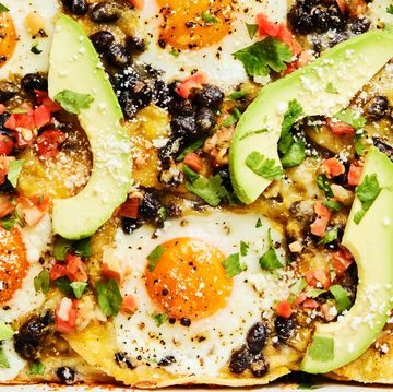 baked casserole with baked eggs, black beans, avocado slices, and tomato chunks on top of tortillas