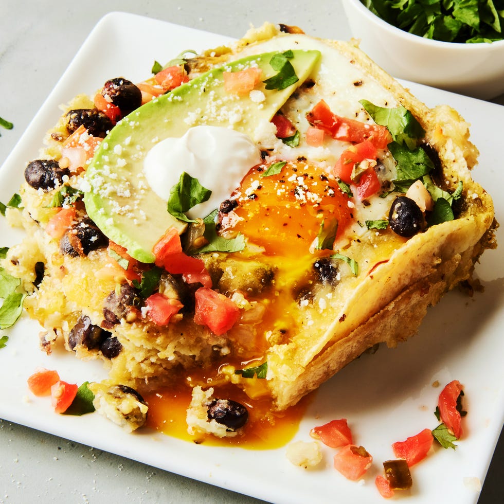 baked casserole with baked eggs, black beans, avocado slices, and tomato chunks on top of tortillas