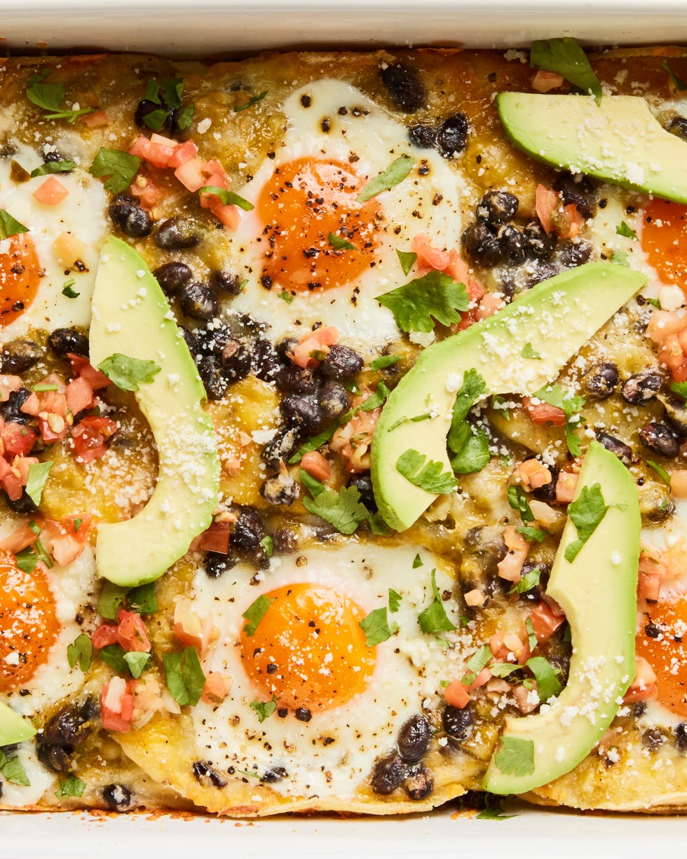 Huevos rancheros casserole in a baking dish topped with sliced ​​avocado, cilantro, and sour cream.