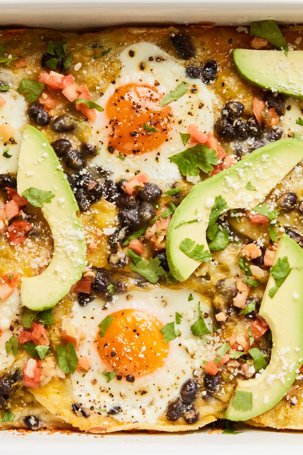 huevos rancheros casserole in a baking dish with topped with sliced avocado, cilantro, and sour cream
