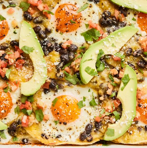huevos rancheros casserole in a baking dish with topped with sliced avocado, cilantro, and sour cream
