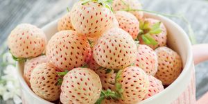 ripe fresh pineberries in a pink cup in a rustic style with small white flowers close up
