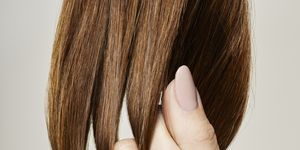 human female hand holding brown hair against gray background, close up