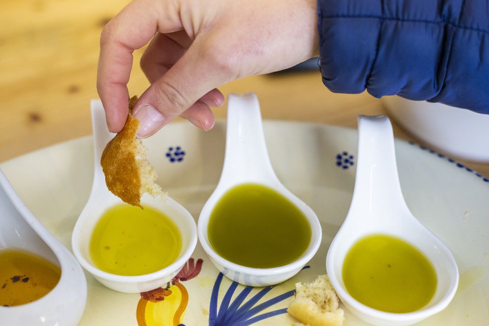 a human hand dips bread in different types of flavored extra virgin olive oils from apulia, italy