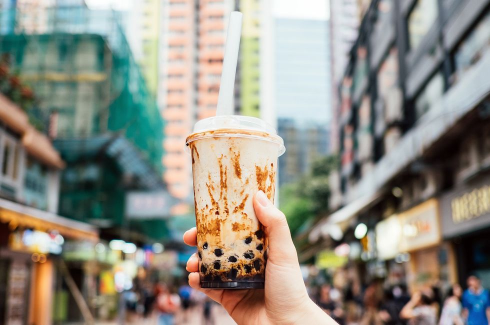 human hand holding a bottle of iced cold bubble tea against city street in a hot summer day