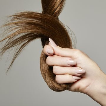 human hand holding brown hair against gray background, close up