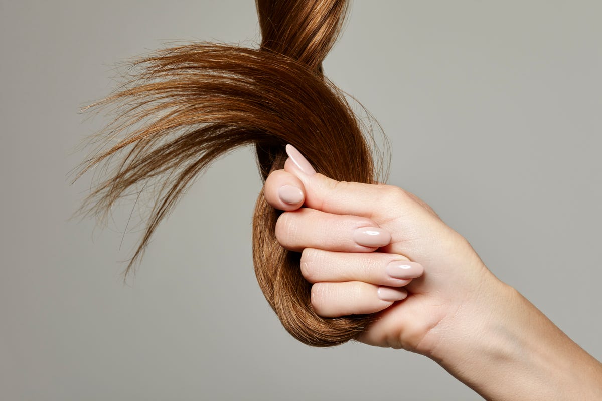 human hand holding brown hair against gray background, close up