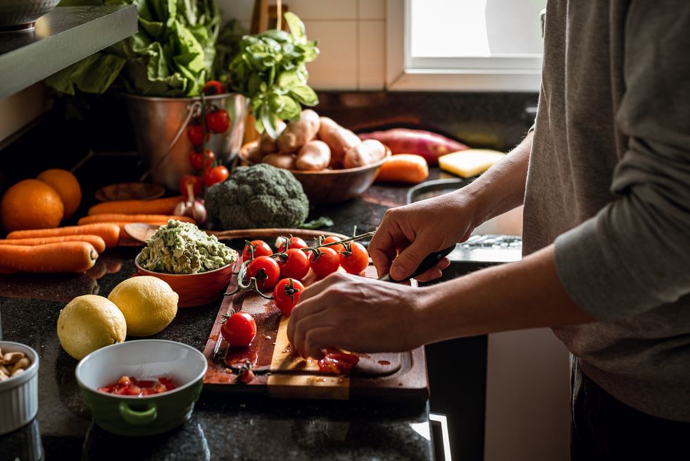 human hands slicing tomatoes over a wooden table for a vegan meal