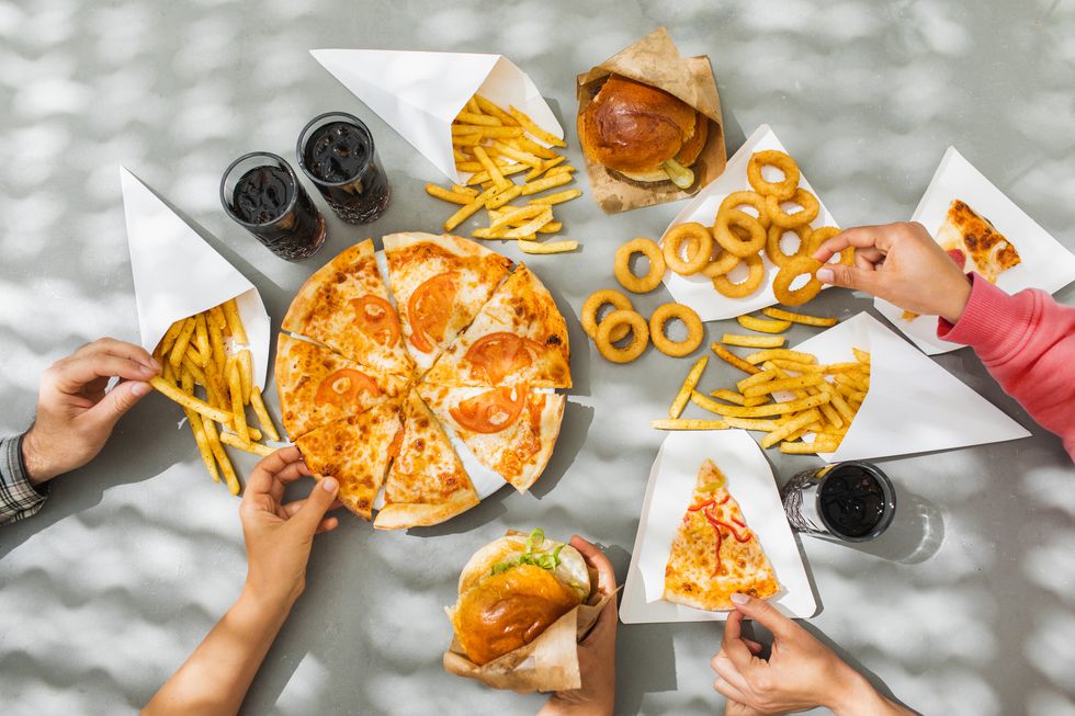 human hands with assorted take out food such as pizza, french fries, onion rings, burger and cola