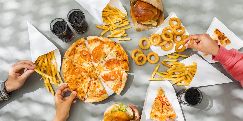 human hands with assorted take out food such as pizza, french fries, onion rings, burger and cola