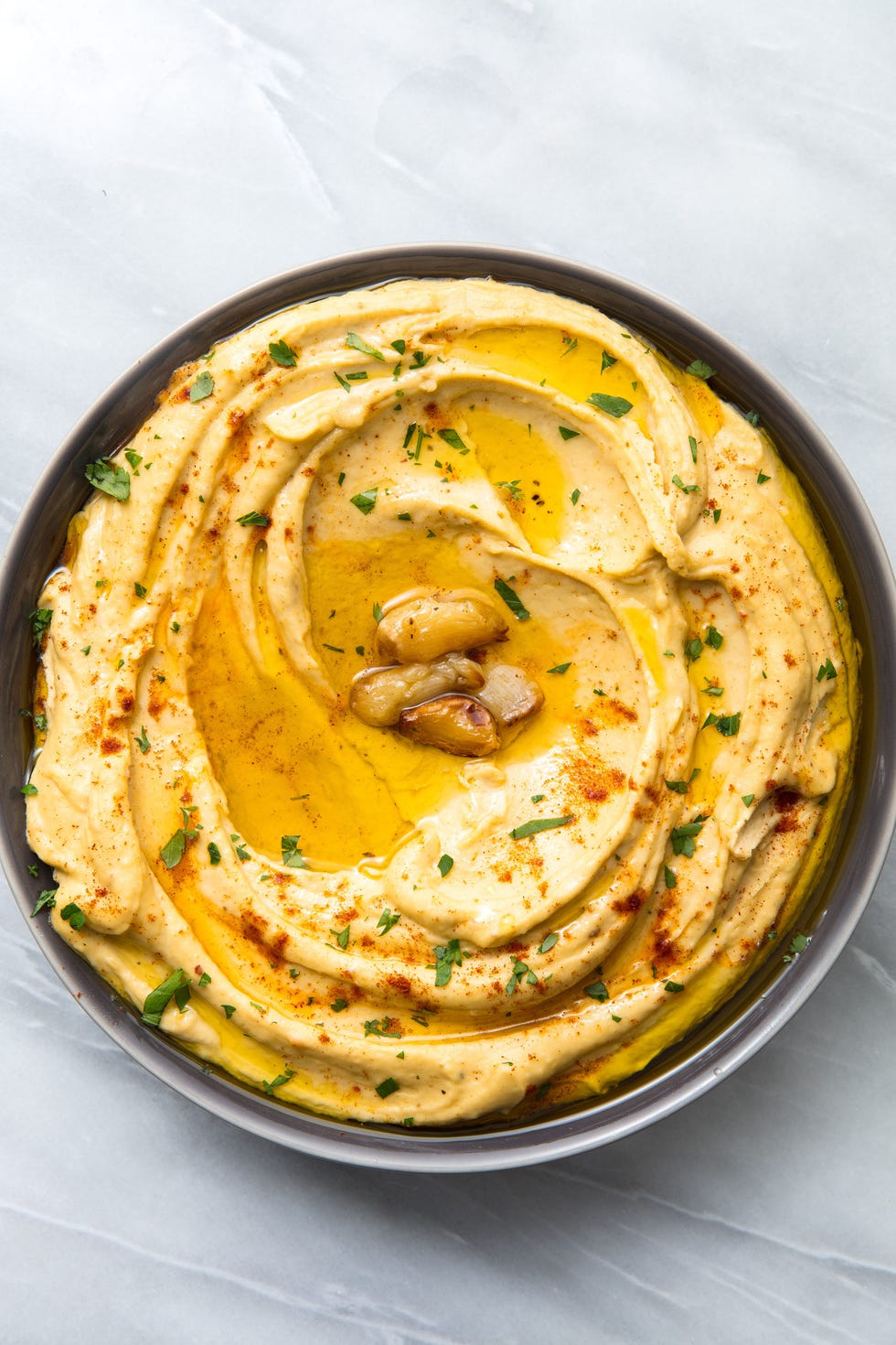 creamy garlic hummus topped with olive oil, roasted garlic, parsley, and paprika in a black bowl