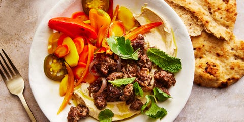 hummus bowl topped with spiced lamb, homemade pickled vegetables, and herbs