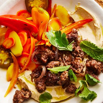 hummus bowl topped with spiced lamb, homemade pickled vegetables, and herbs