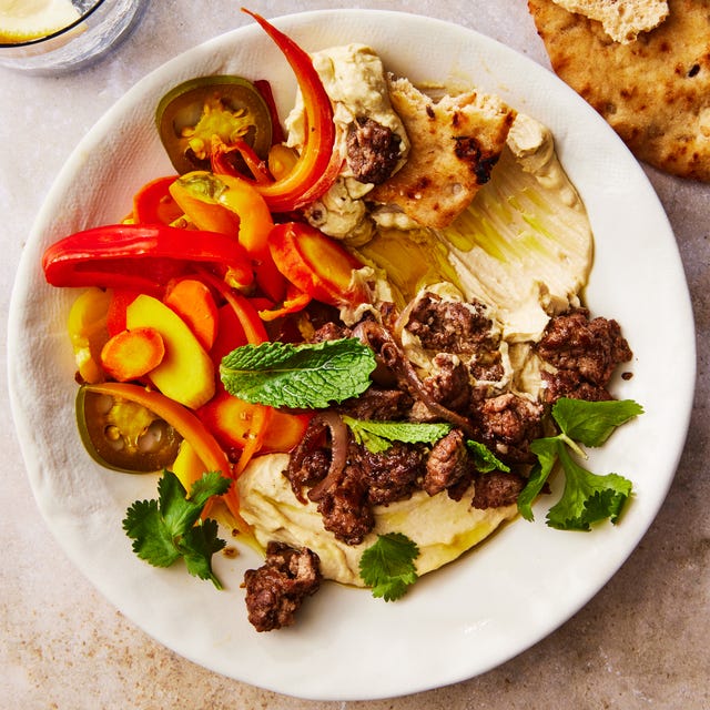 hummus bowl topped with spiced lamb, homemade pickled vegetables, and herbs